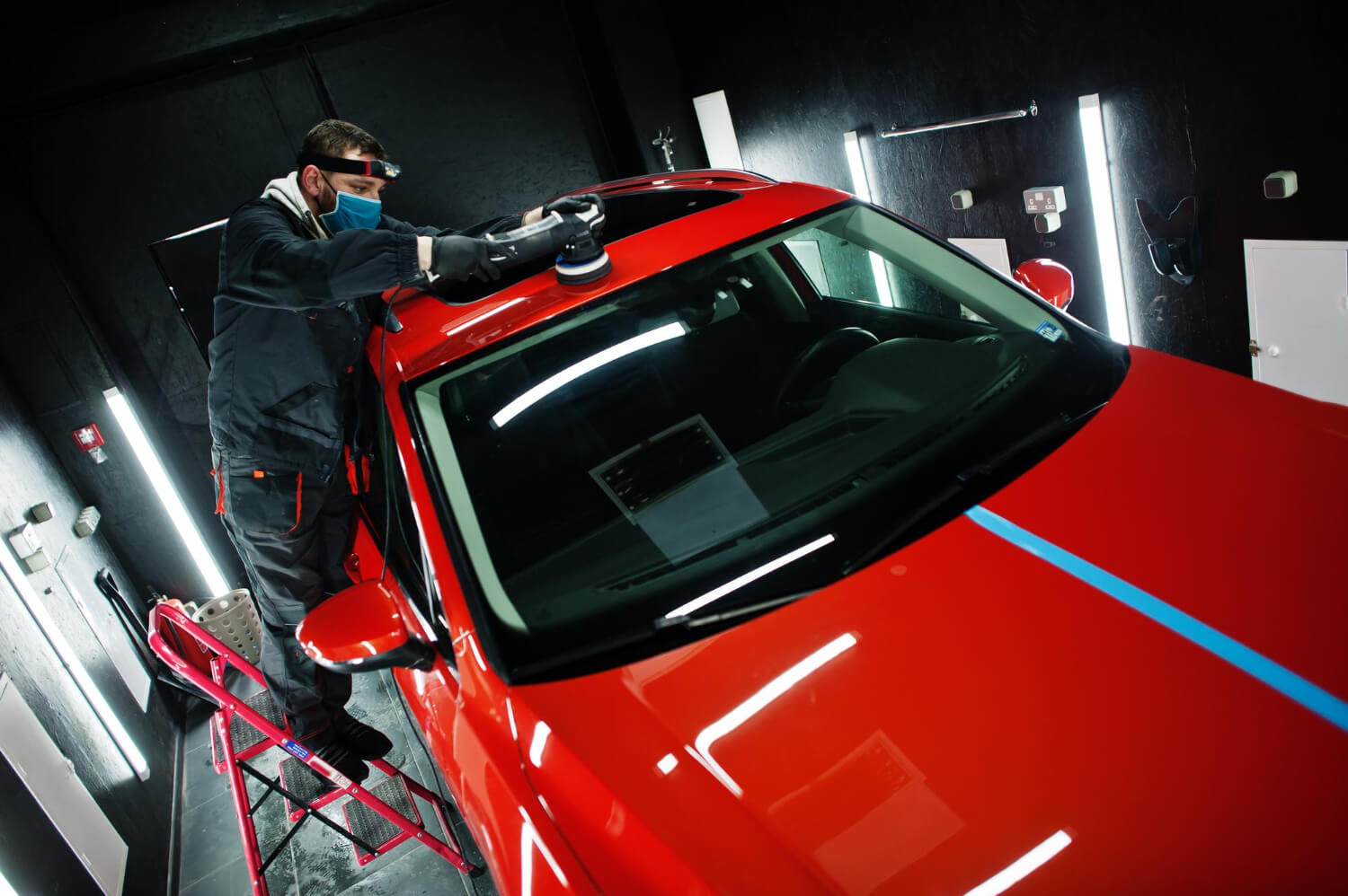 Tecnico mentre lucida la carrozzeria di un’auto rossa con lucidatrice elettrica in officina professionale, per ottenere una superficie brillante e senza graffi