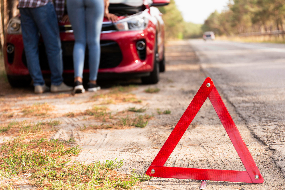 Una coppia accanto a un'auto rotta con un triangolo rosso di emergenza posizionato sulla strada.