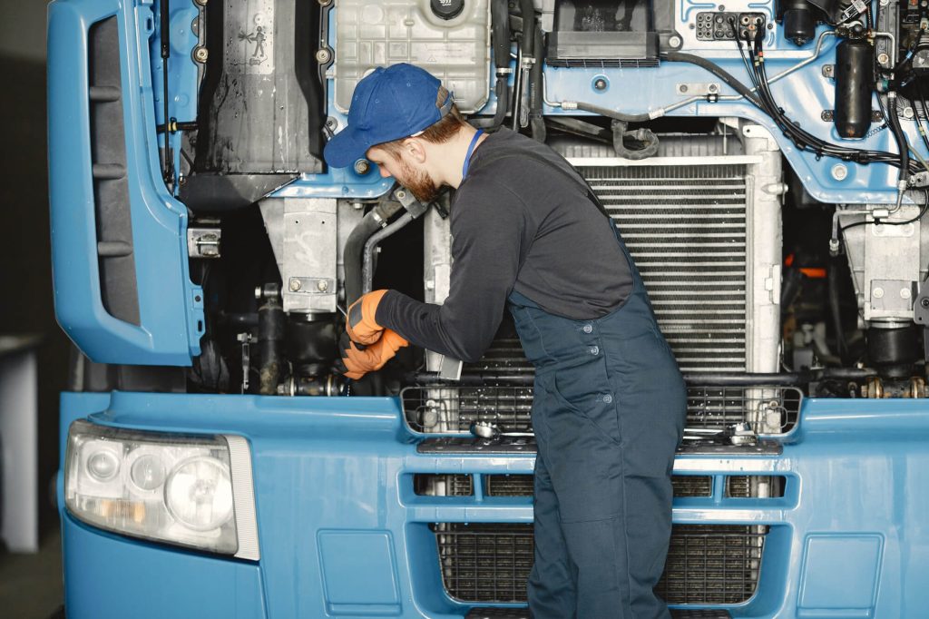 Un uomo in tuta da lavoro ripara un grande camion nel garage