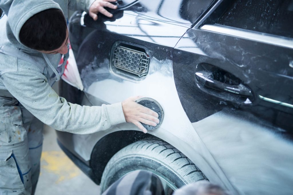 Un uomo applica vernice nera su un'auto in fase di riparazione