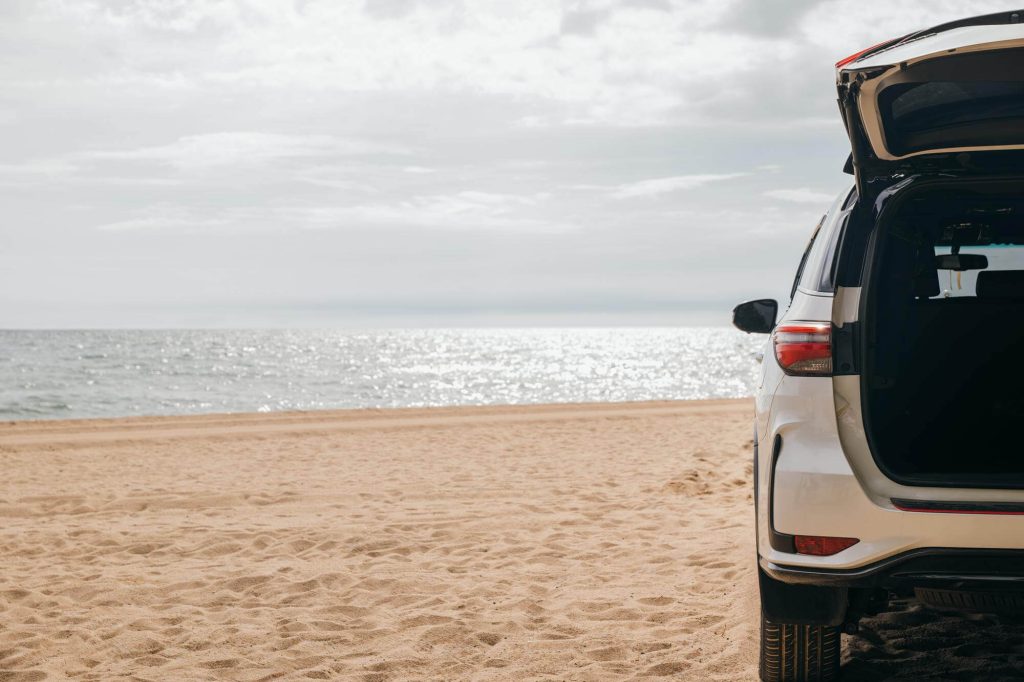 Un'auto bianca parcheggiata sulla spiaggia, con il bagagliaio aperto e il mare sullo sfondo